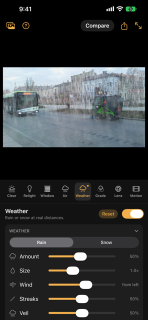 Weather on a town street: rain falling behind a bus and a street sweeper, thicker toward the buildings